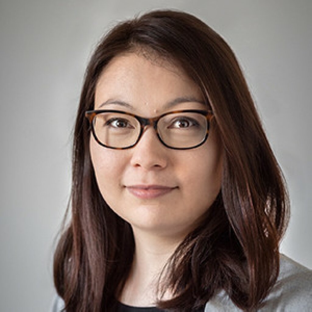 Larissa lächelt in die Kamera. Sie trägt eine Brille und offenes, schulterlanges, braun-rötliches Haar.